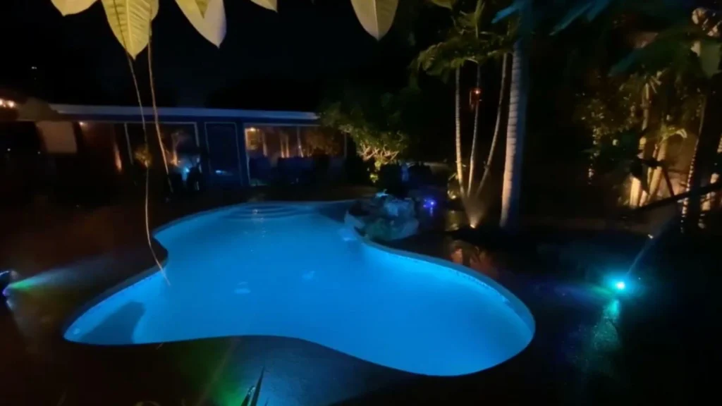 Backyard pool illuminated at night with landscape lighting