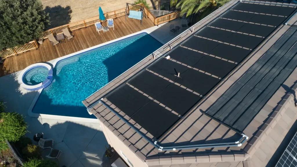 Roof-mounted solar pool heating panels installed above a backyard pool