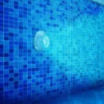 Blue underwater pool light illuminating tiled pool wall