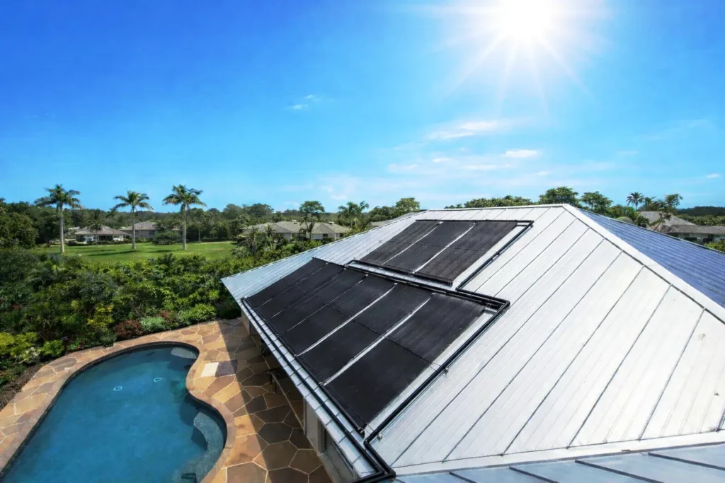 Solar pool heating panels installed on a residential metal roof overlooking a backyard pool